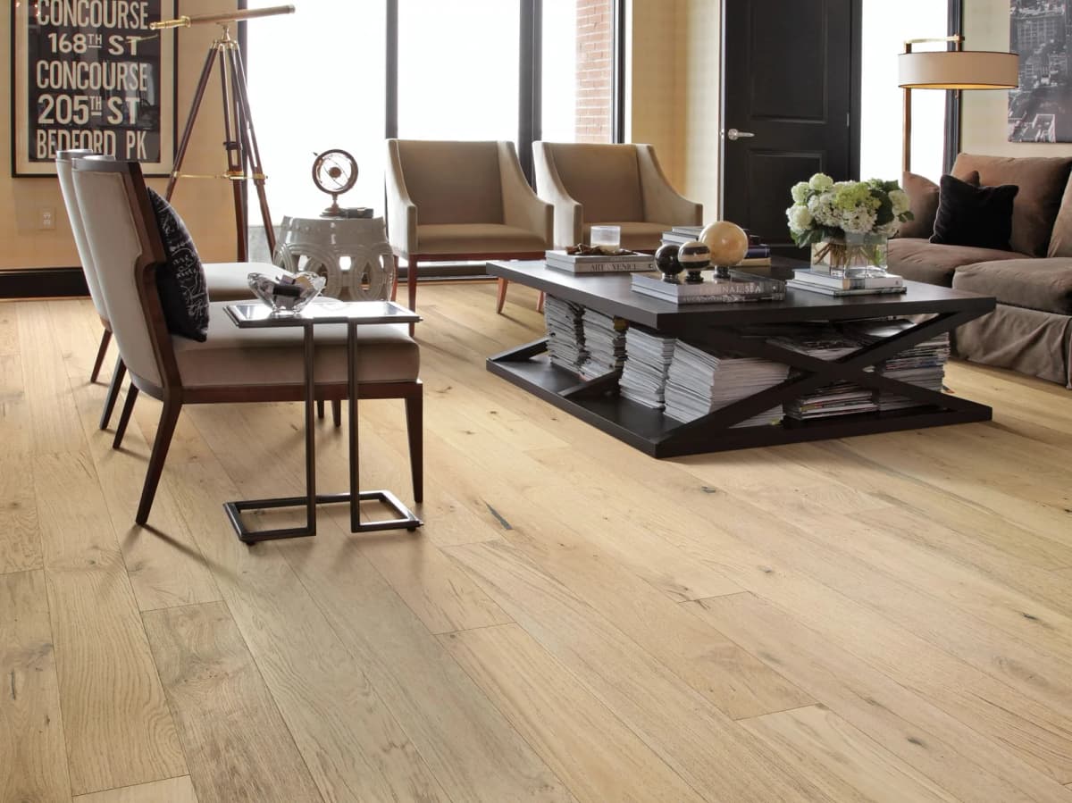Wide-plank white oak engineered hardwood flooring in a bright loft-style living room with cream upholstered chairs and a dark wood coffee table