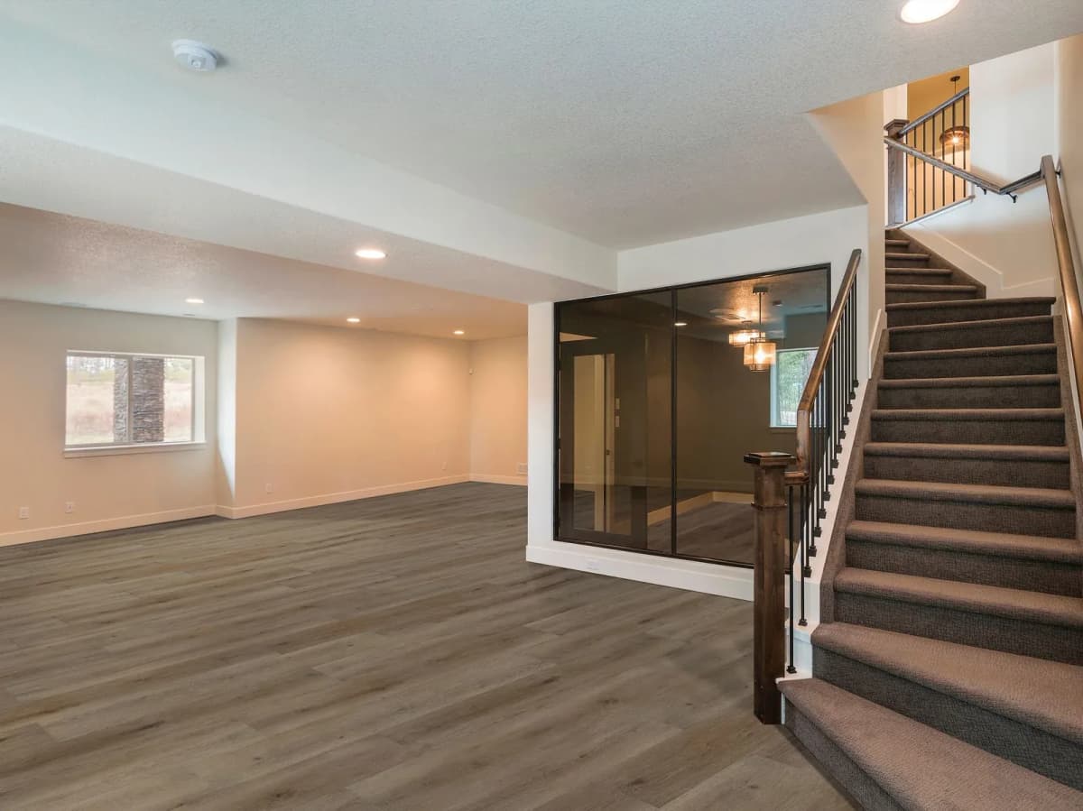Wood-look luxury vinyl plank flooring spans a finished basement rec room, with a carpeted staircase, a glass-walled room, and recessed ceiling lighting