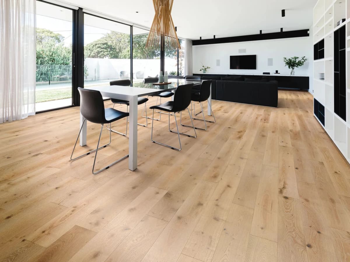 Open-plan dining and living room with wide light-oak plank flooring running toward floor-to-ceiling glass doors onto a garden